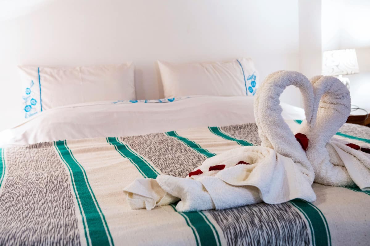 Cama bem arrumada com manta listrada e duas toalhas dispostas em forma de coração.