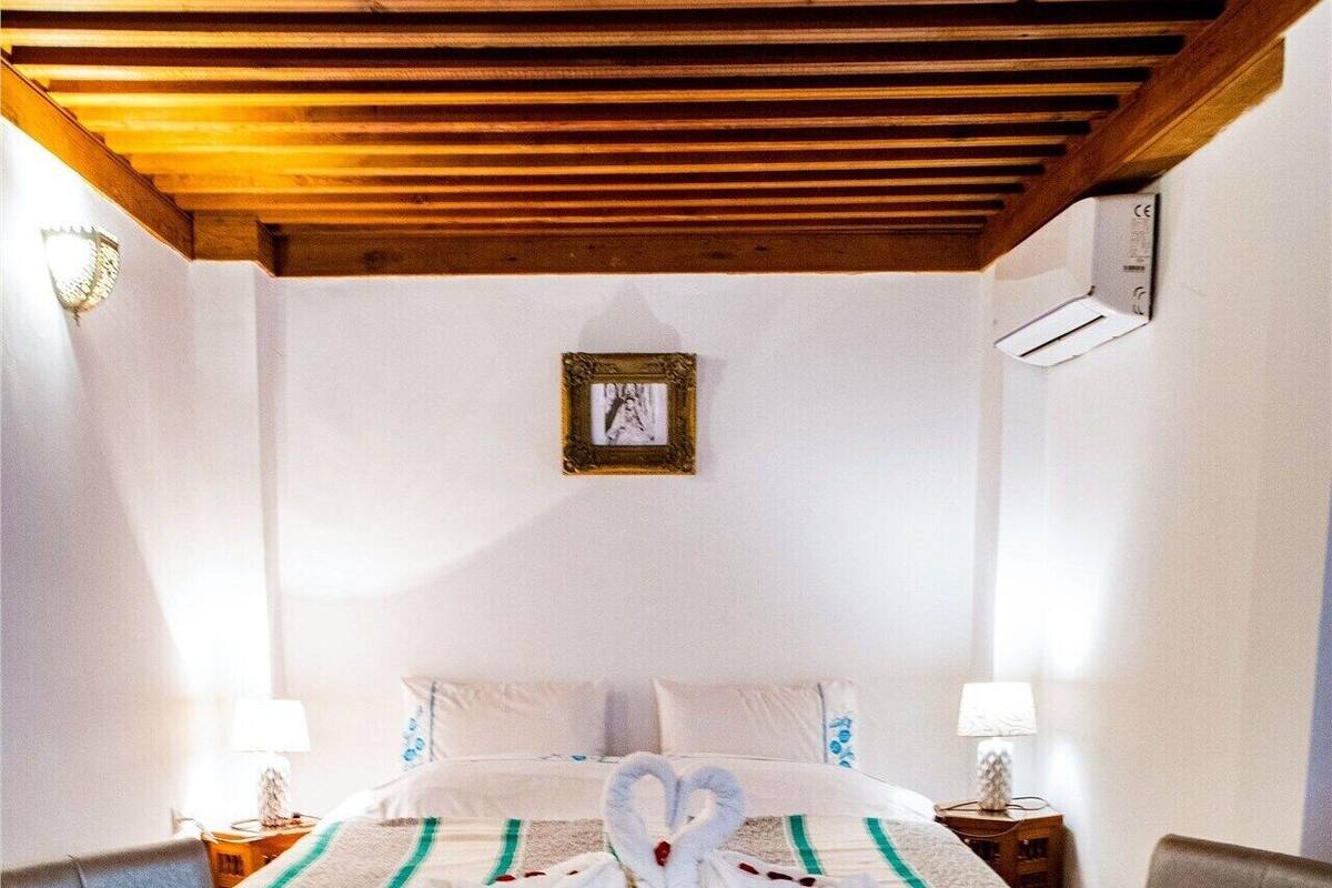 Quarto com cama, duas poltronas, uma mesinha e um tapete estampado.