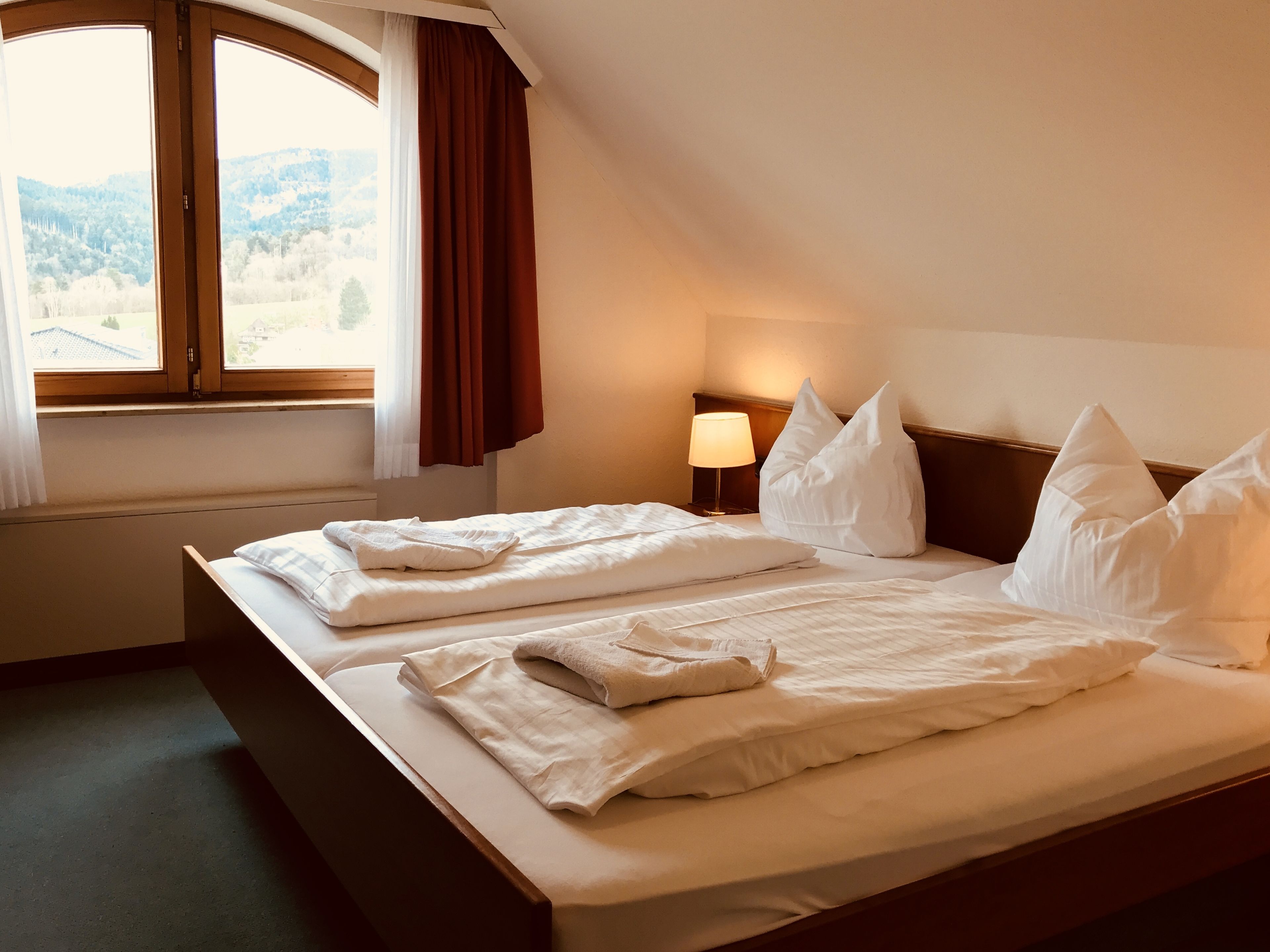 Ein Hotelzimmer mit einem großen Bett, einer Nachttischlampe und Blick auf eine gebirgige Landschaft durch ein Fenster.