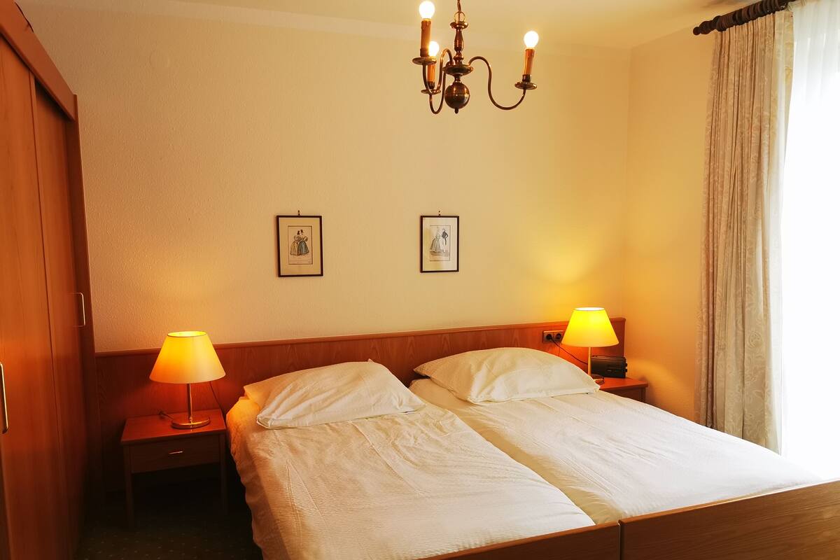 Una cama doble con dos mesitas de noche, cada una con una lámpara, en una habitación con cabecera de madera y un candelabro.