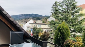 Ein Balkon mit Glastisch, Blumentöpfen und Blick auf Gebäude und Hügel.