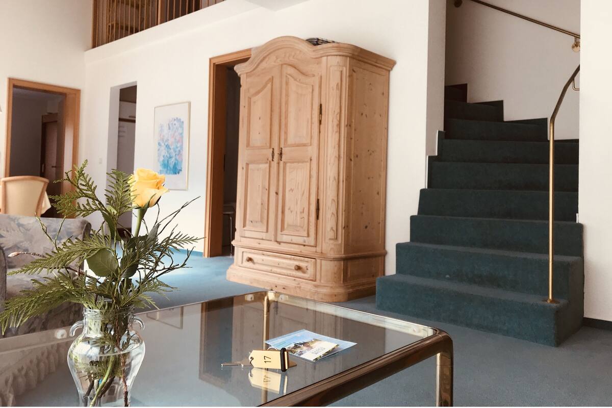 Un amplio salón con una mesa de centro de vidrio, un mueble de madera y una escalera.