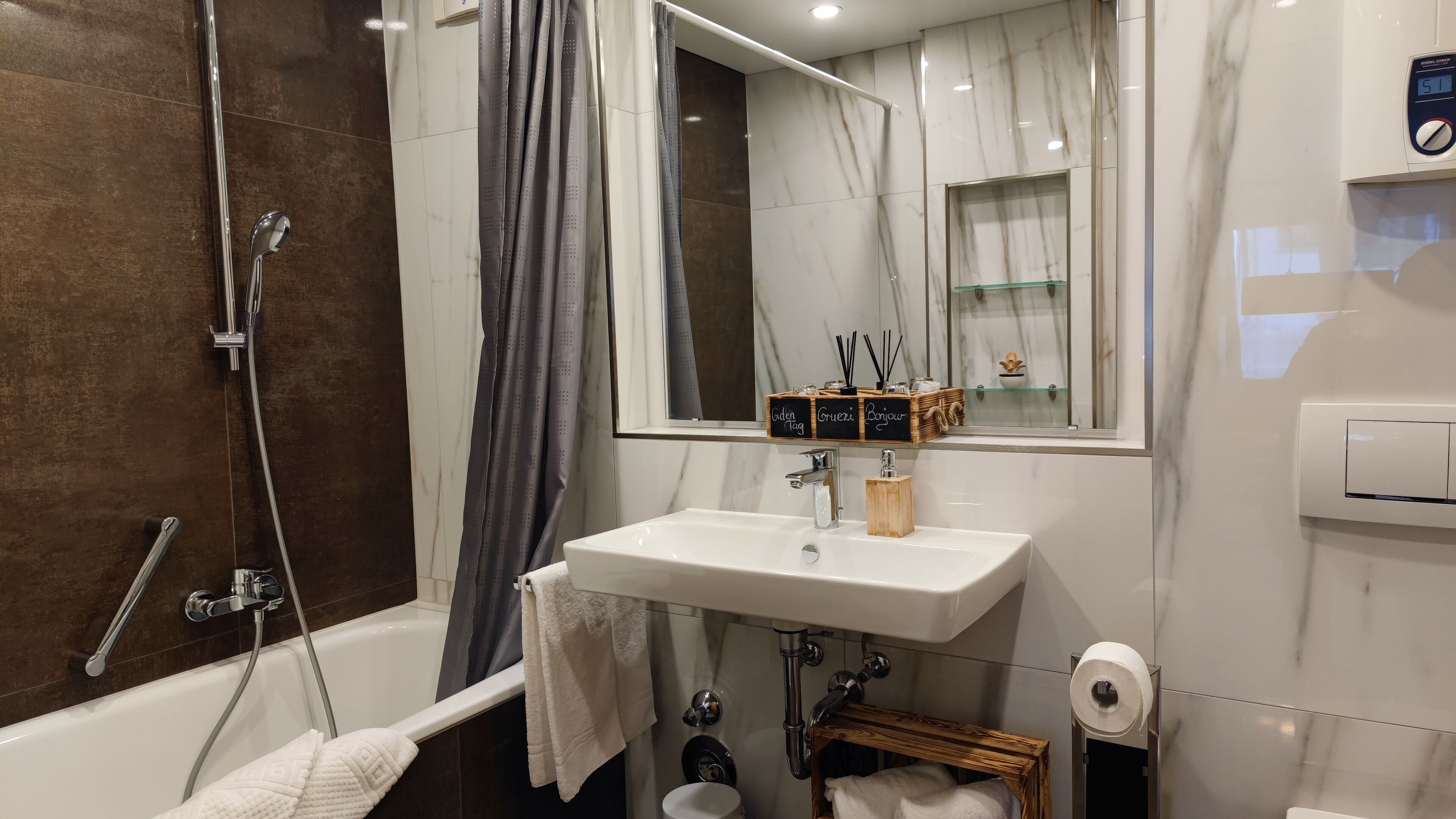 A modern bathroom with a bathtub, a shower, a sink, and a toilet. There is a mirror above the sink and a window with a view of the outside.