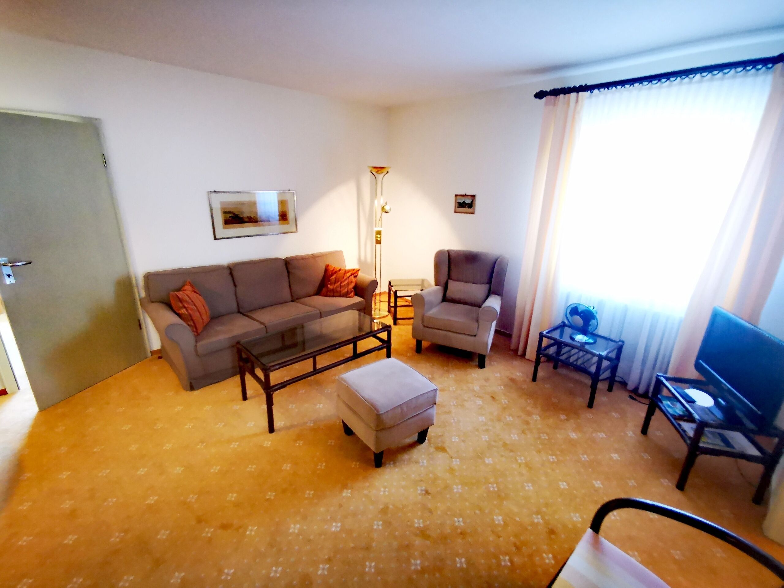 Una sala de estar con sofá, sillón, reposapiés, una mesa de centro y televisor sobre un mueble.