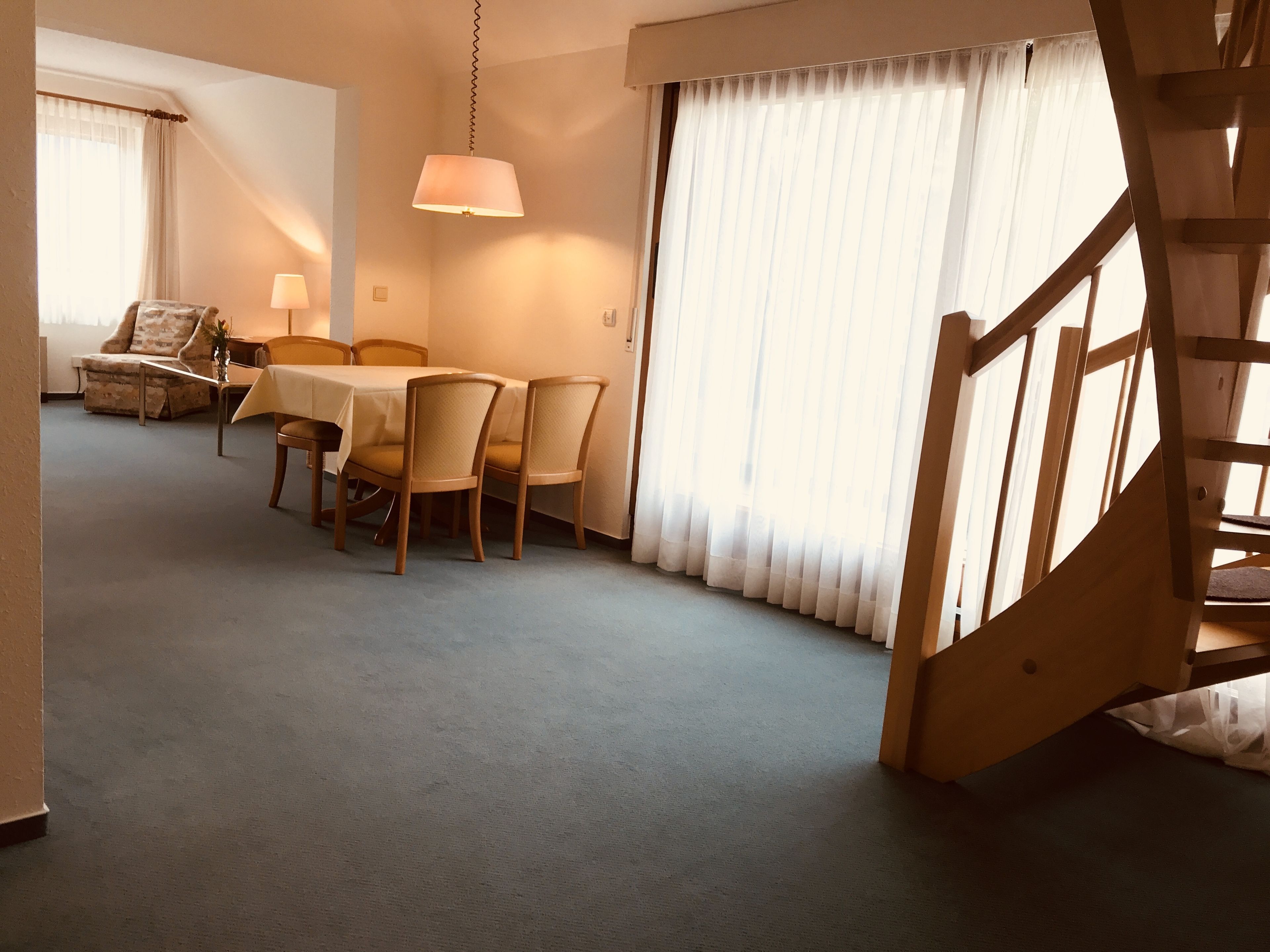 A room with a dining table, chairs, a lamp, a sofa, and a staircase.