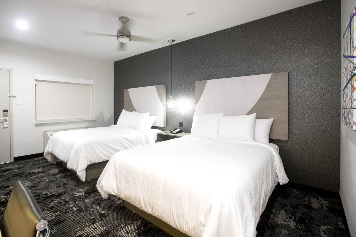 Camera d'albergo con due letti, una ventola a soffitto, un comodino con una lampada e un tappeto decorato.