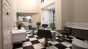 Un vestíbulo con piso a cuadros, zonas de estar, un mostrador de recepción y un candelabro moderno.