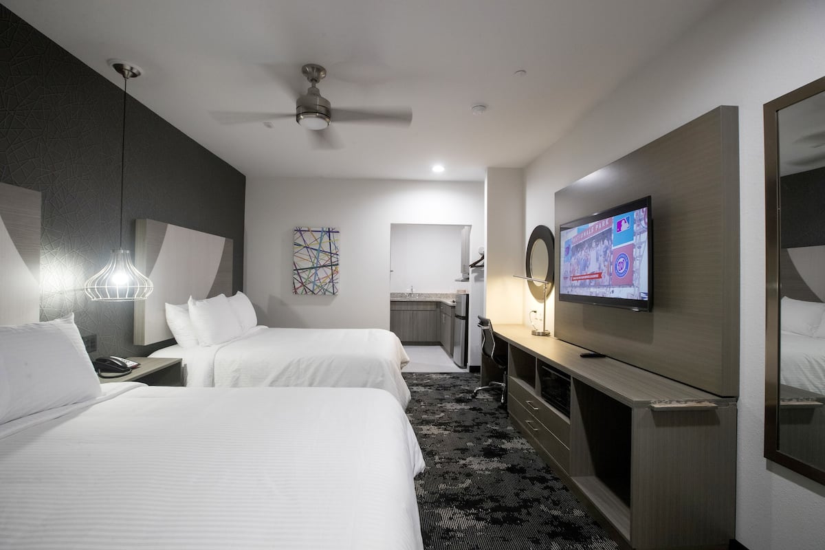 Camera d'albergo con due letti, una televisione, una scrivania e un bagno sullo sfondo.
