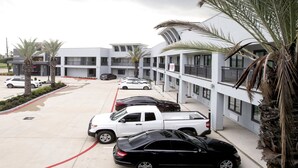 Un hotel de varios pisos con un diseño arquitectónico moderno, con balcones y un estacionamiento con varios autos.