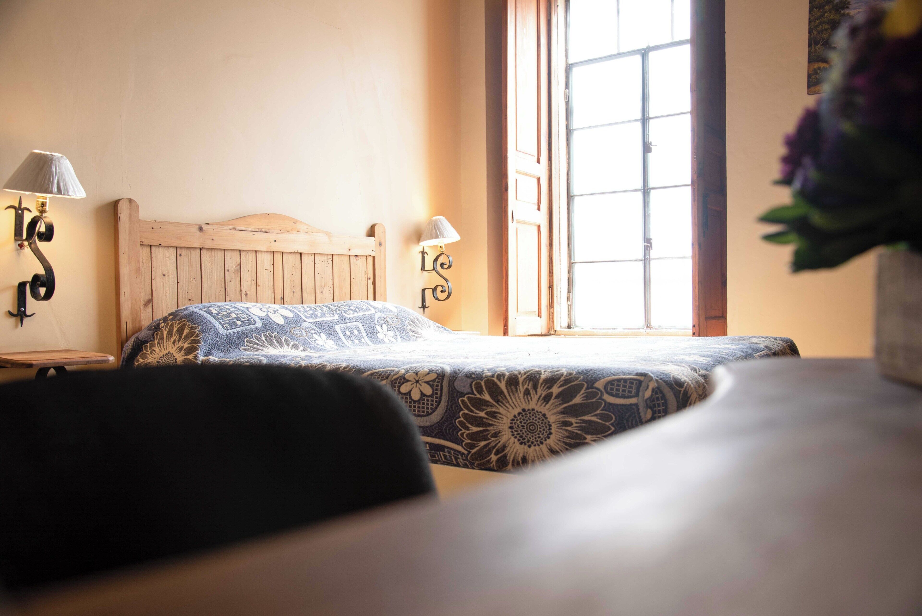 A bed with a wooden headboard, two bedside lamps, and a window with a view.