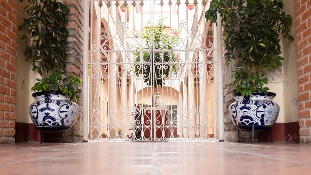 A corridor with a wrought iron gate, potted plants, and a brick wall. - Hotel Rincón Poblano (Puebla)