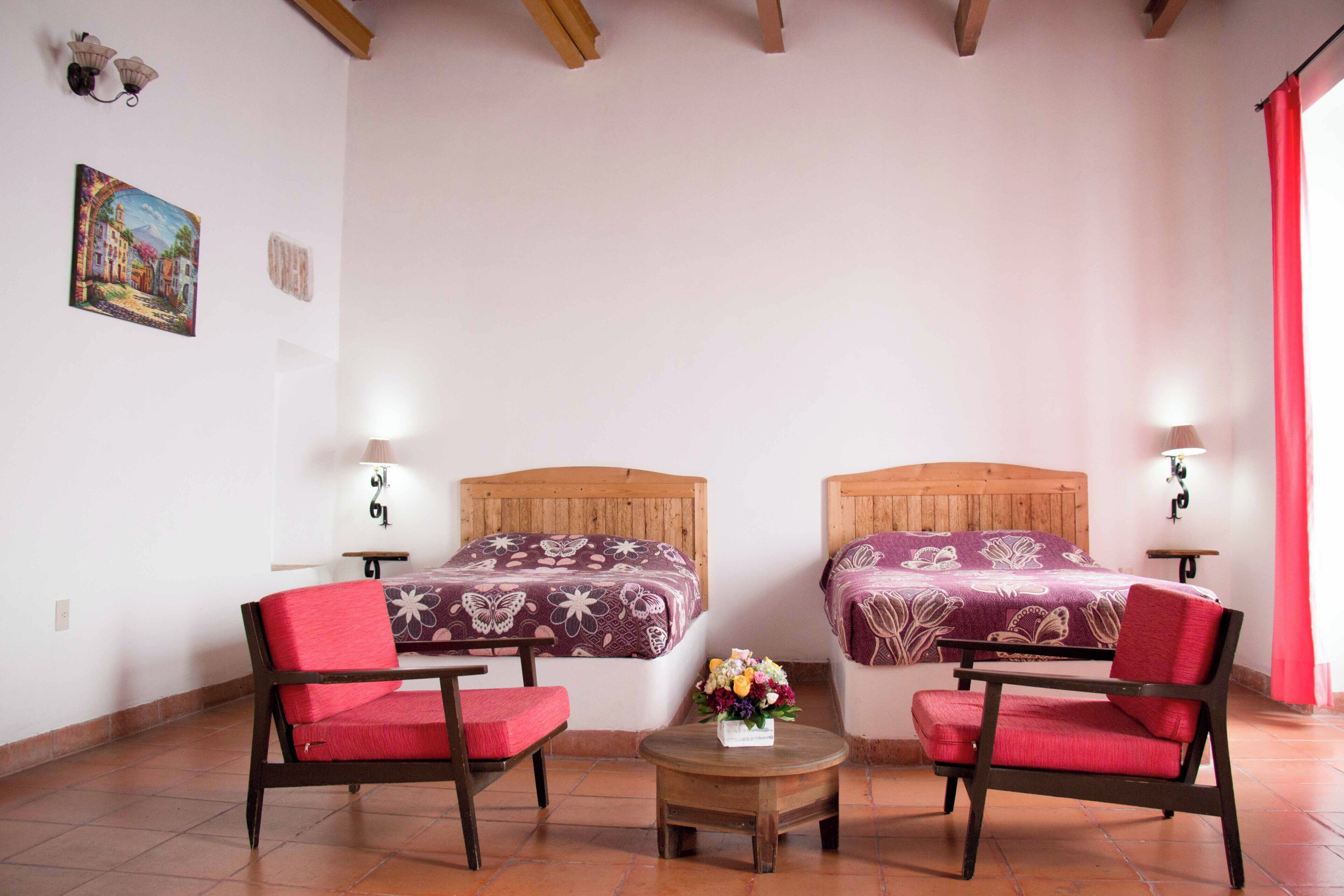 A room with two beds, a small table with a vase of flowers, and two chairs.