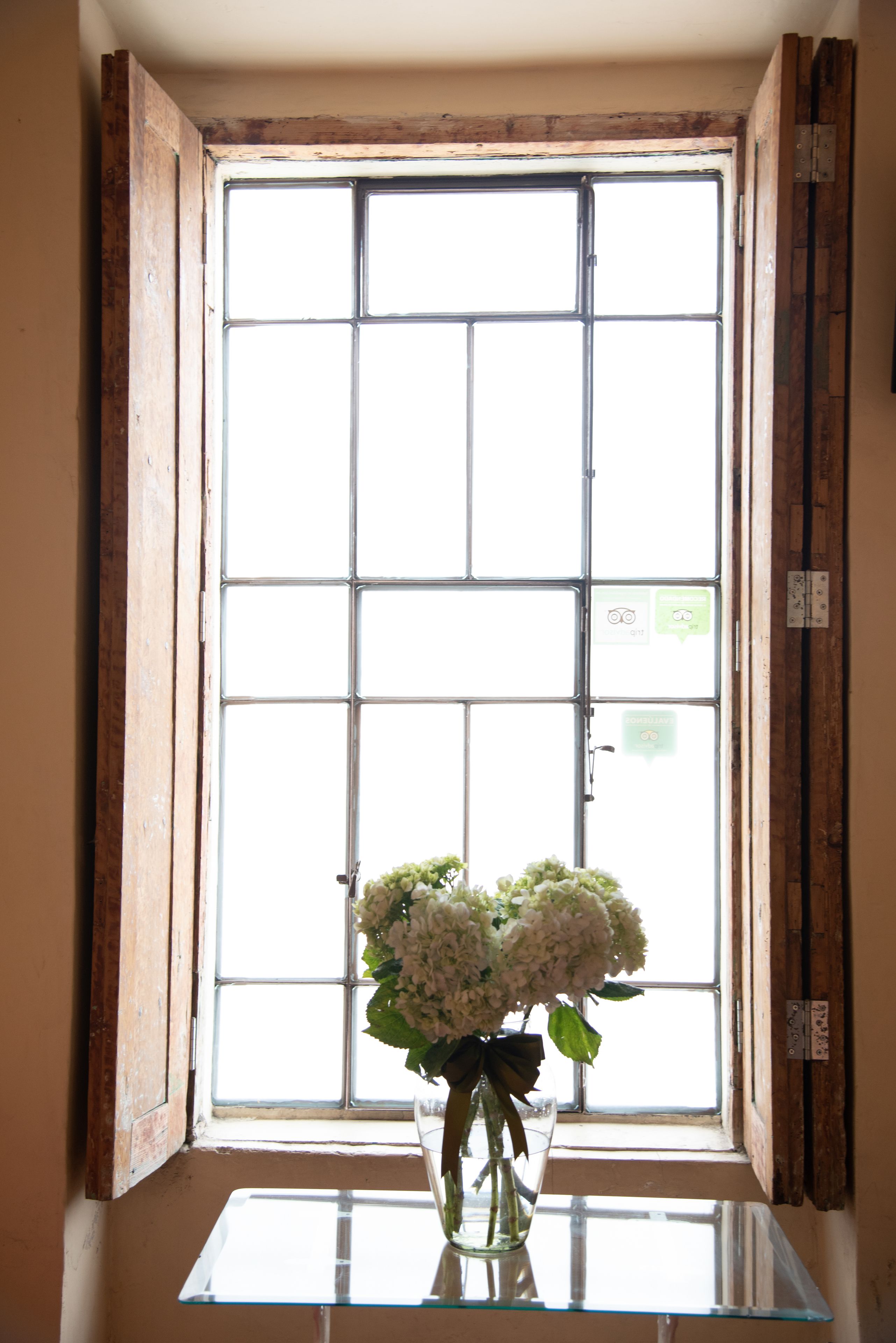 Une fenêtre avec un cadre en bois et une table en verre sur laquelle est posé un vase de fleurs.