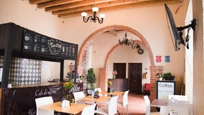 A café with a rustic interior, featuring exposed brick arches, a coffee bar, and white chairs. - Hotel Rincón Poblano (Puebla)
