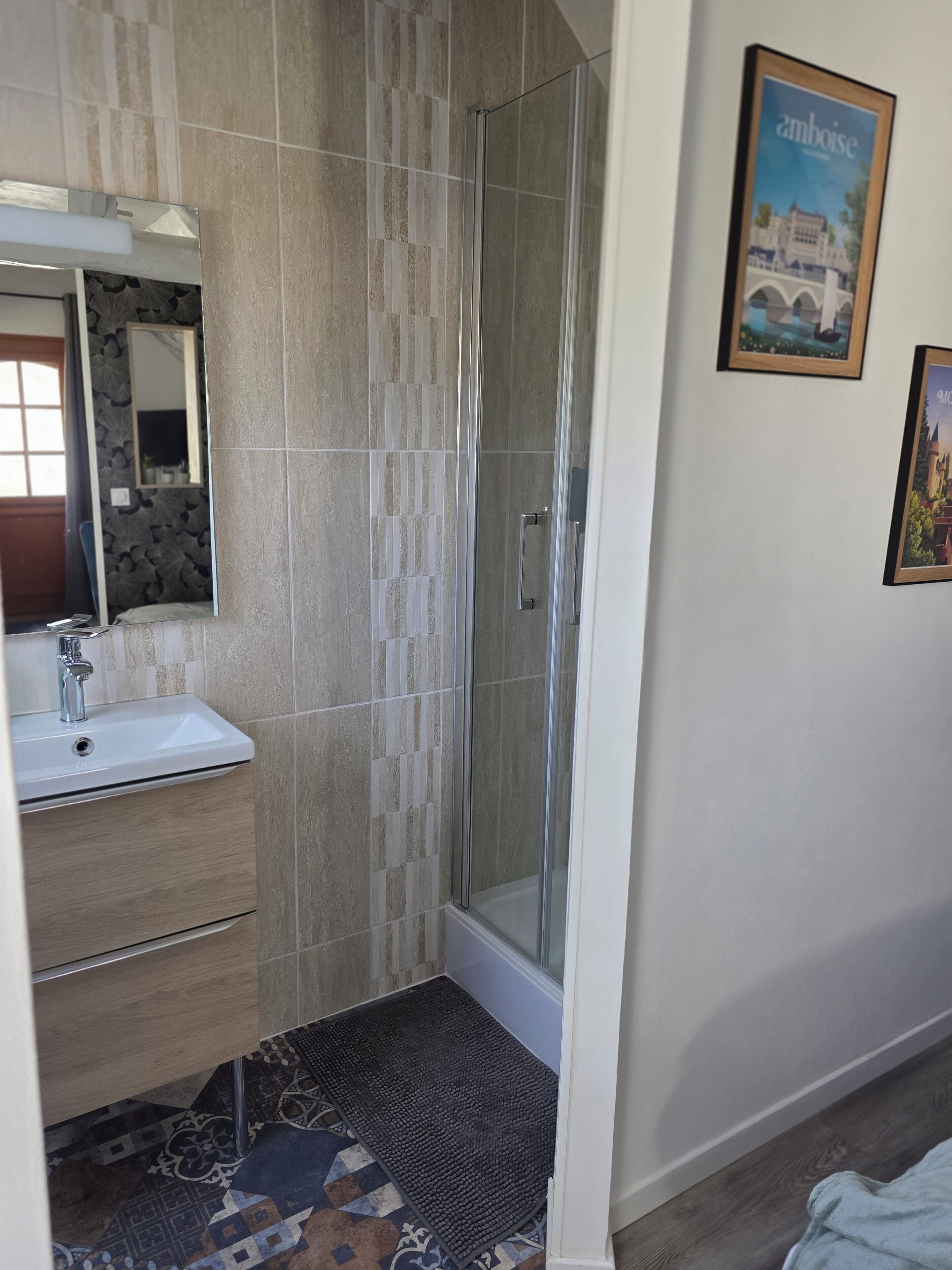 Un baño con cabina de ducha de vidrio, un lavabo con espejo y un felpudo estampado.