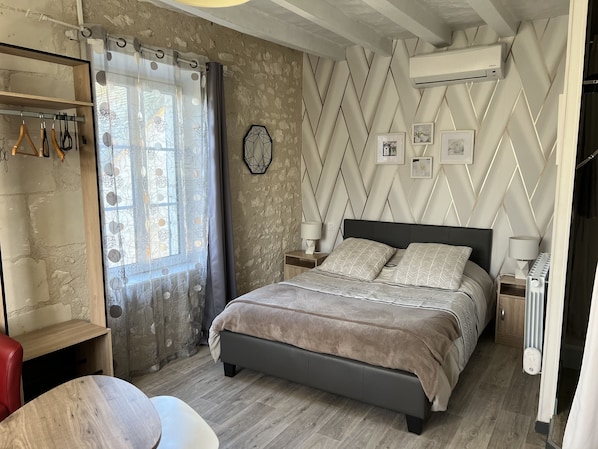 A bedroom with a bed, a nightstand, a lamp, a radiator, a window with curtains, and a wall with a geometric pattern. - Chambres des Coteaux (Sainte-Maure-de-Touraine)