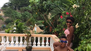 A balcony with a tiled floor, surrounded by lush greenery and flowering plants. - Mountain Top Villa (Mandeville)
