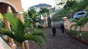 A gated entrance with palm trees and a paved pathway leading to a building. - Mountain Top Villa (Mandeville)