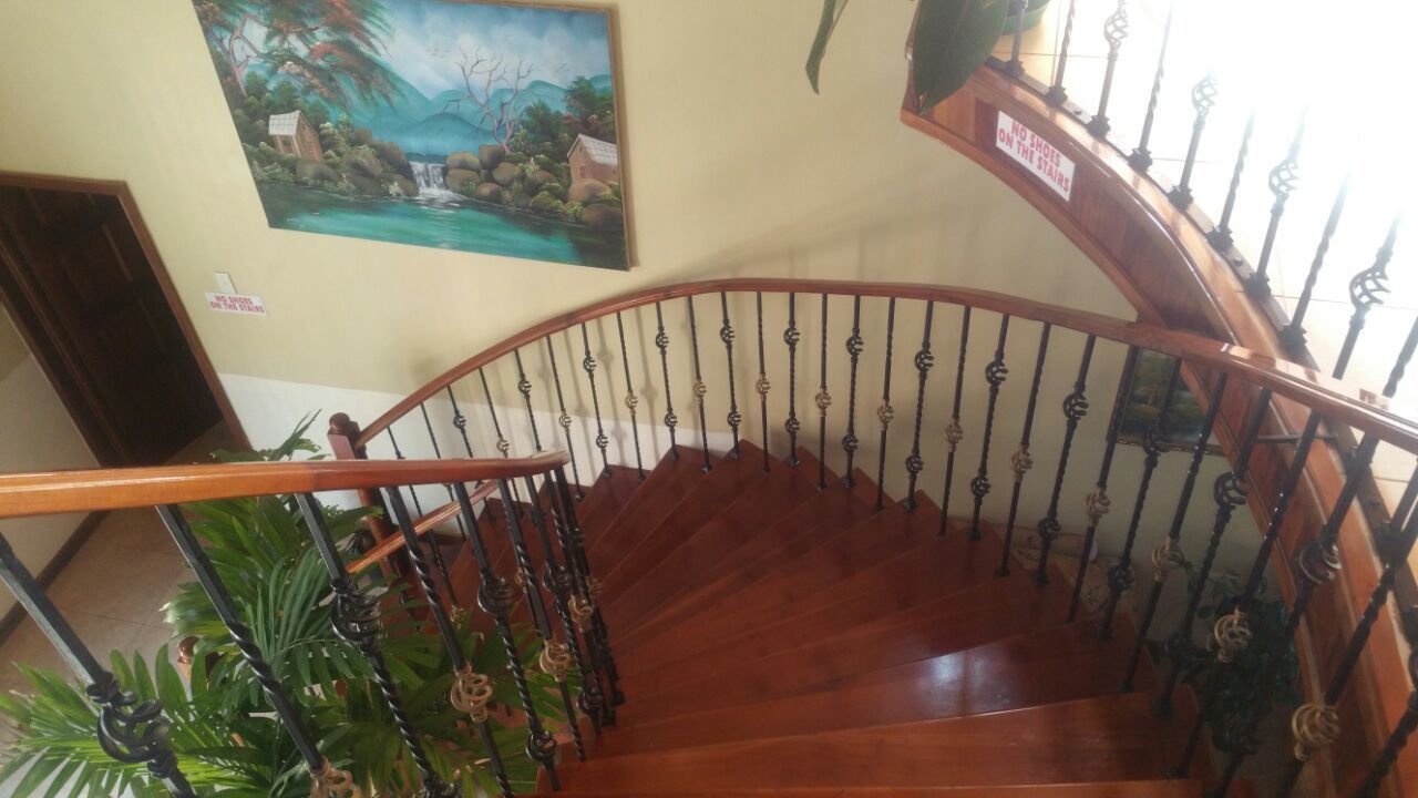 Un escalier en bois, agrémenté de rampes noires décorées, et un tableau représentant un paysage tropical accroché au mur.