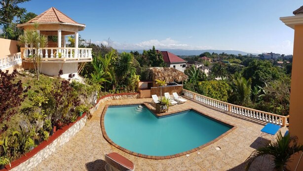 A pool area with a gazebo, lounge chairs, and a view of the surrounding landscape. - Mountain Top Villa (Mandeville)