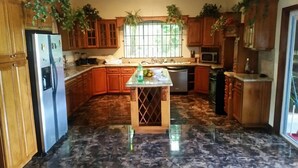 A kitchen with wooden cabinets, a marble floor, a central island, and a window with plants. - Mountain Top Villa (Mandeville)