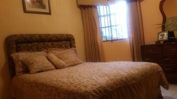 A bed with a patterned bedspread, a dresser with a mirror, and a window with curtains.