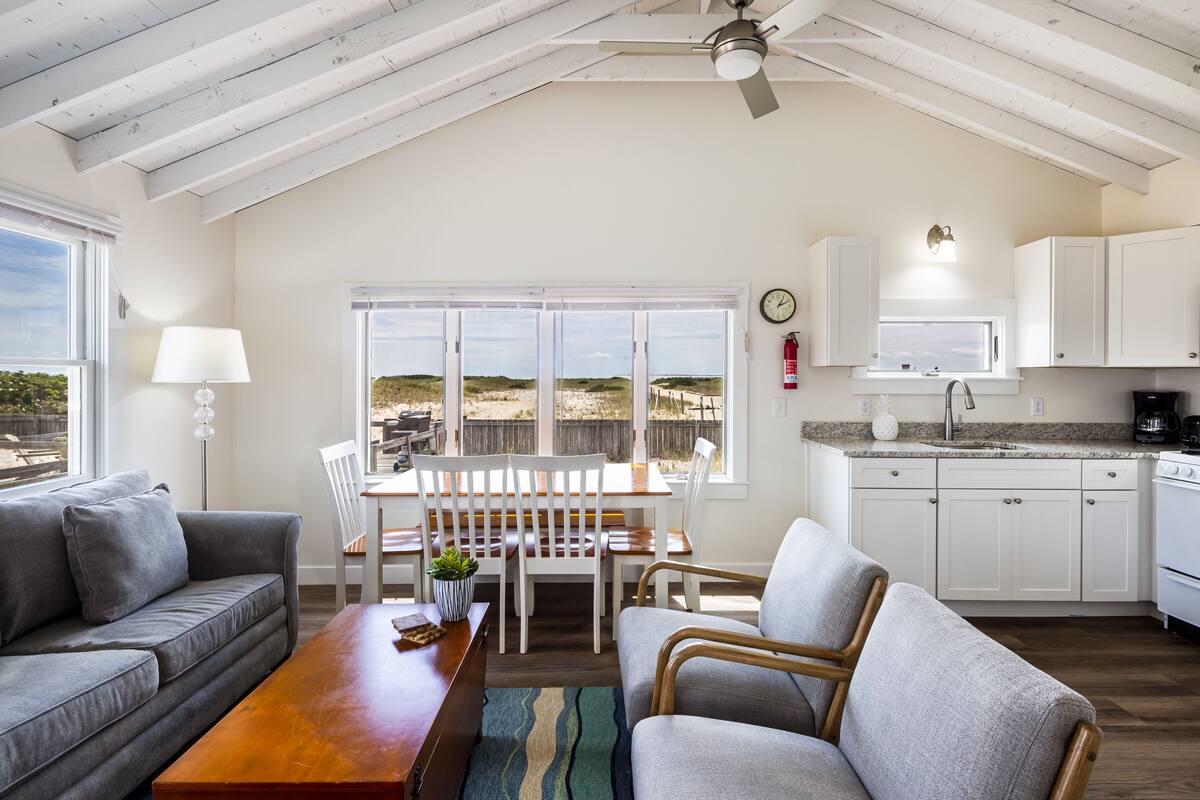 A spacious living room with a high ceiling, a dining area with a view, and a kitchen with white cabinets.