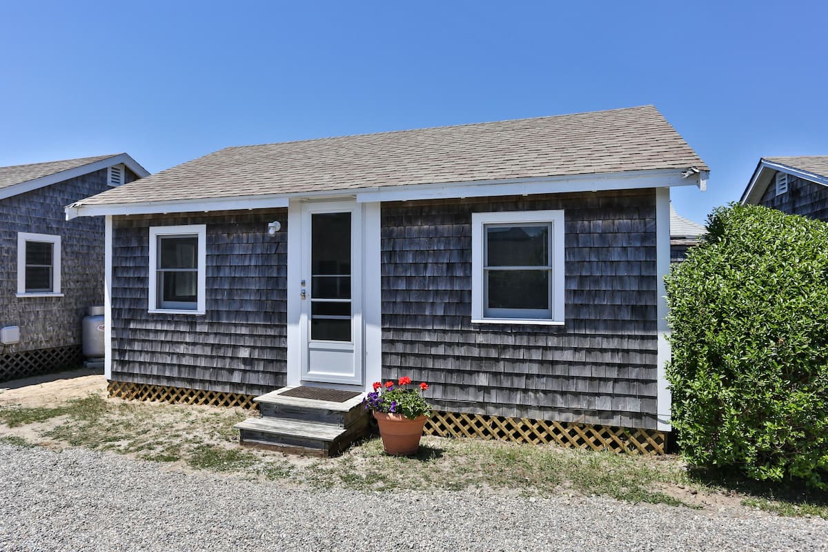 A single-story house with a shingled exterior, a front door, two windows, and a small porch.