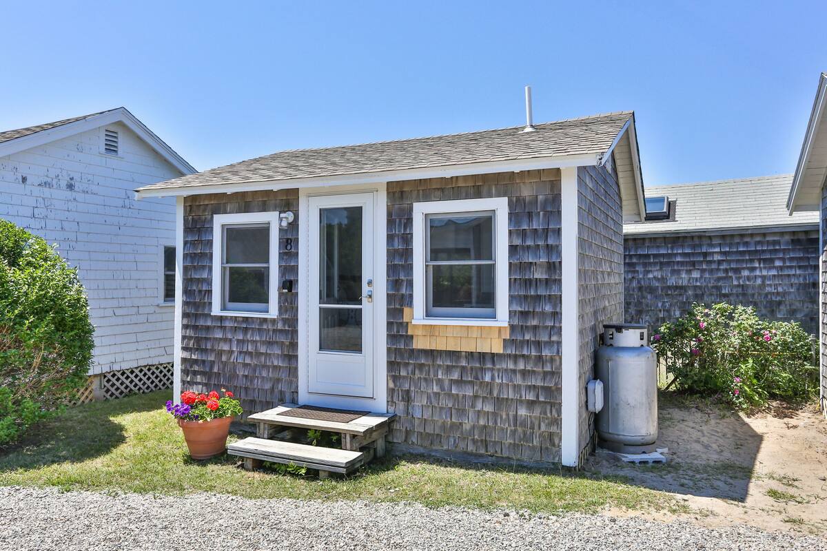 A small, single-story house with a front door, two windows, and a small porch.