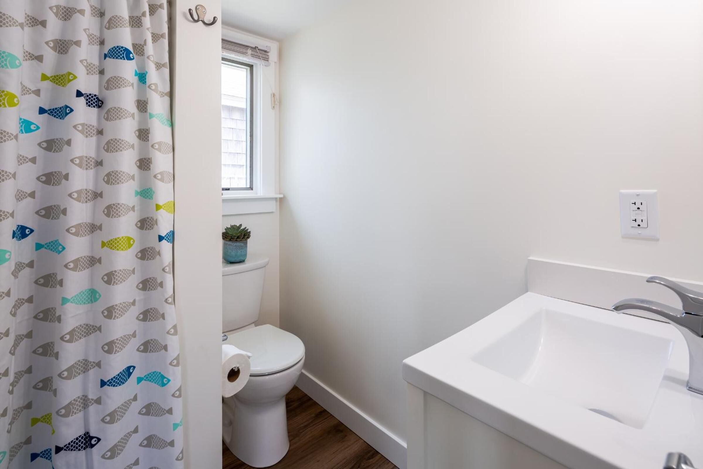 Un baño con inodoro, lavamanos y ventana sobre el inodoro.