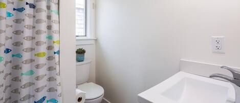 Un baño con inodoro, lavamanos y ventana sobre el inodoro.