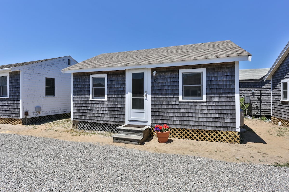A small, single-story mobile home with a front door, two windows, and a small porch with steps.