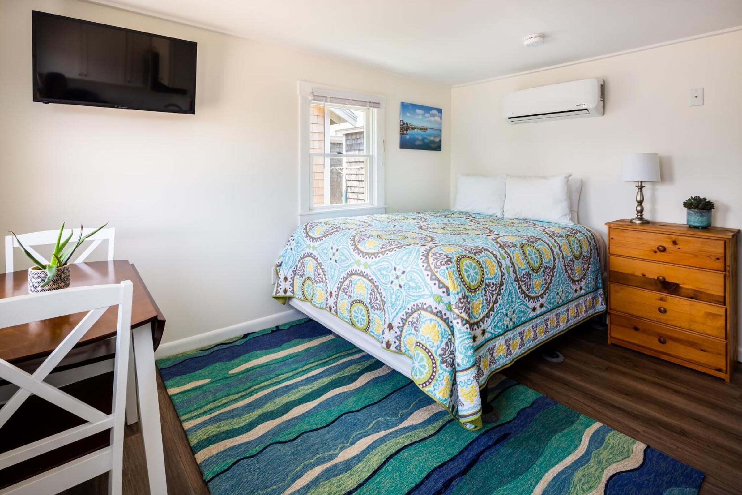 A bedroom with a bed, a desk, a chair, a dresser, a TV, and an air conditioner.