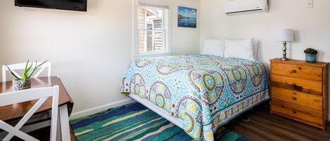 A bedroom with a bed, a desk, a chair, a dresser, a TV, and an air conditioner.