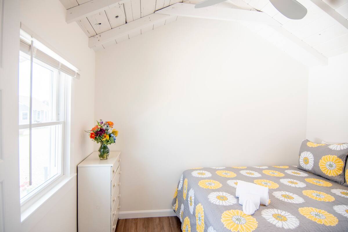 A bedroom with a bed, a dresser, a window, and a ceiling with exposed beams.