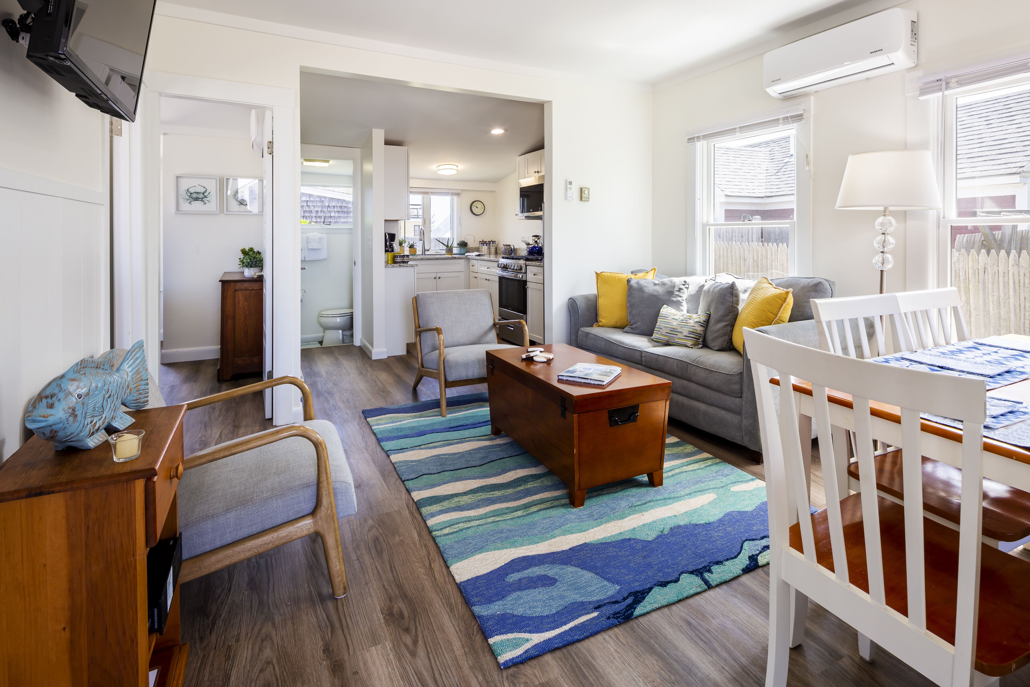 Una sala moderna con sofá, una mesa de centro y una mesa de comedor con sillas. Se observa una cocina al fondo con refrigerador y estufa.