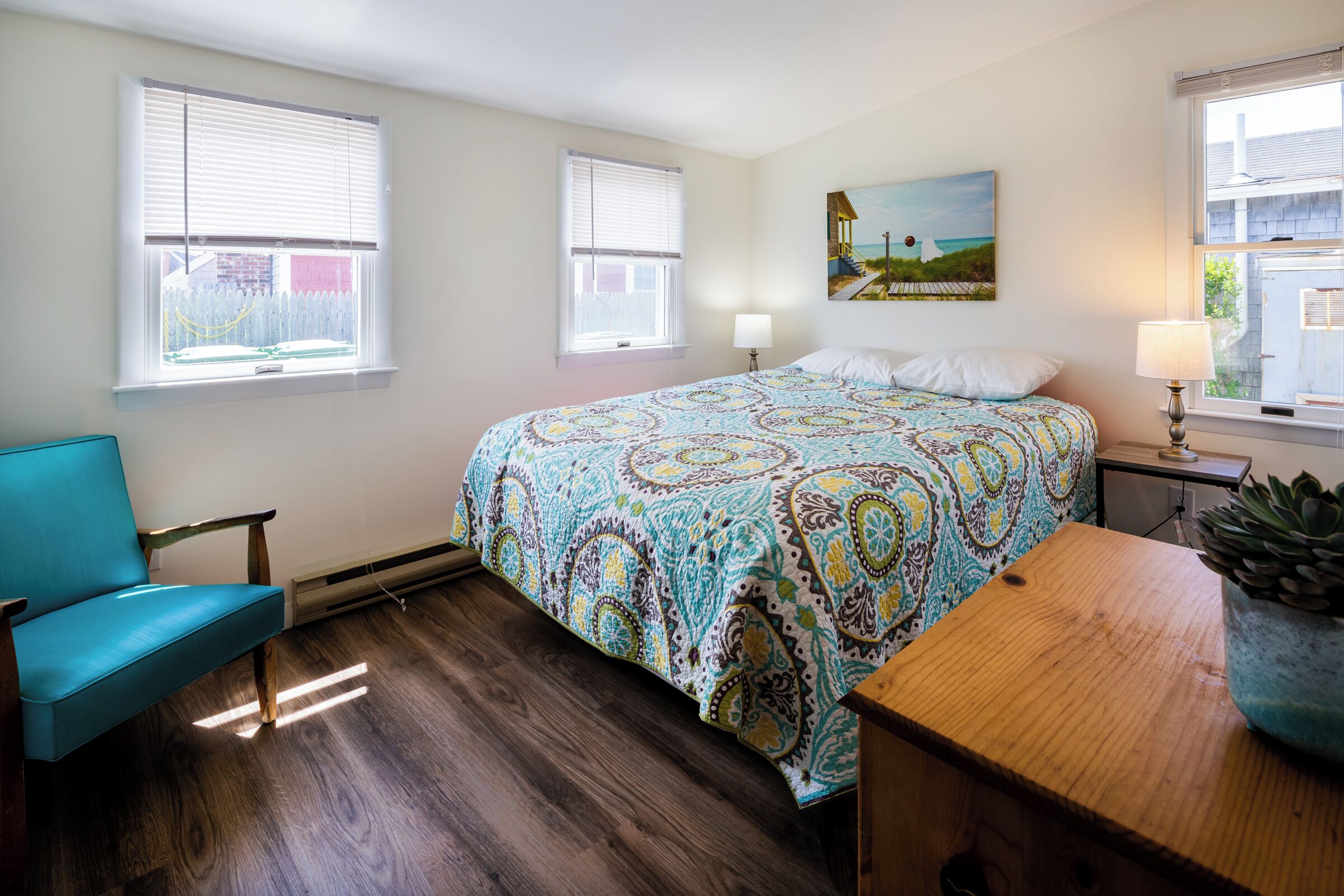 A bedroom with a bed, a chair, a nightstand, a lamp, and a painting on the wall.