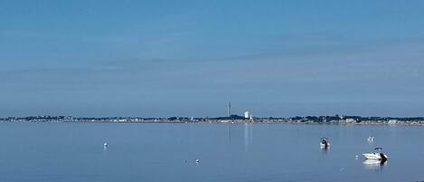 A calm waterfront with boats, a distant tower, and a clear sky.