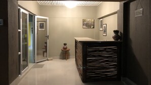 Un pasillo con una puerta de vidrio que da a una habitación, una mesita con un florero y un cuadro en la pared.