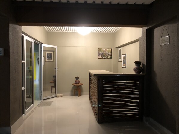 Un pasillo con una puerta de vidrio que da a una habitación, una mesita con un florero y un cuadro en la pared.
