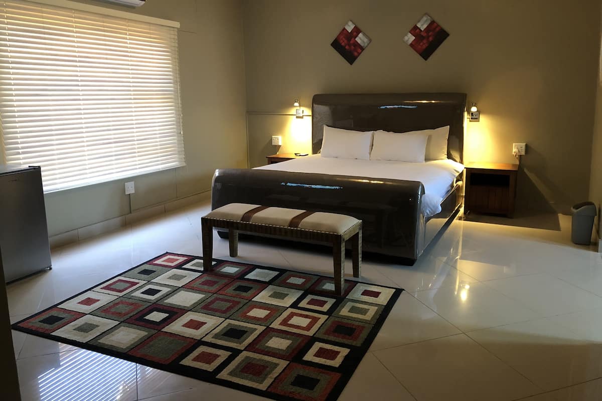 A bedroom with a bed, bedside tables, a bench, a rug, and a wall-mounted air conditioner.