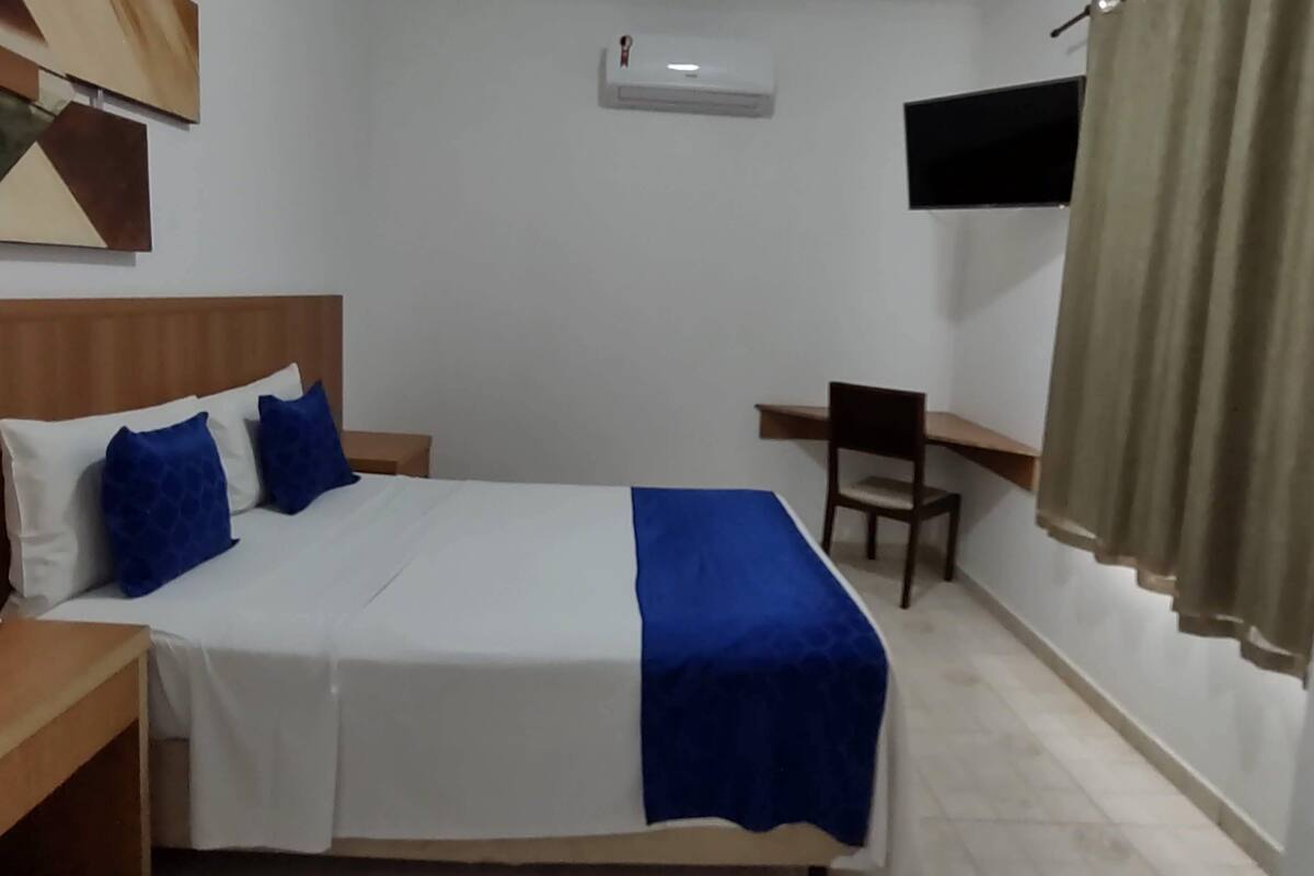 Una habitación de hotel con cama, escritorio, silla y televisión montada en la pared.