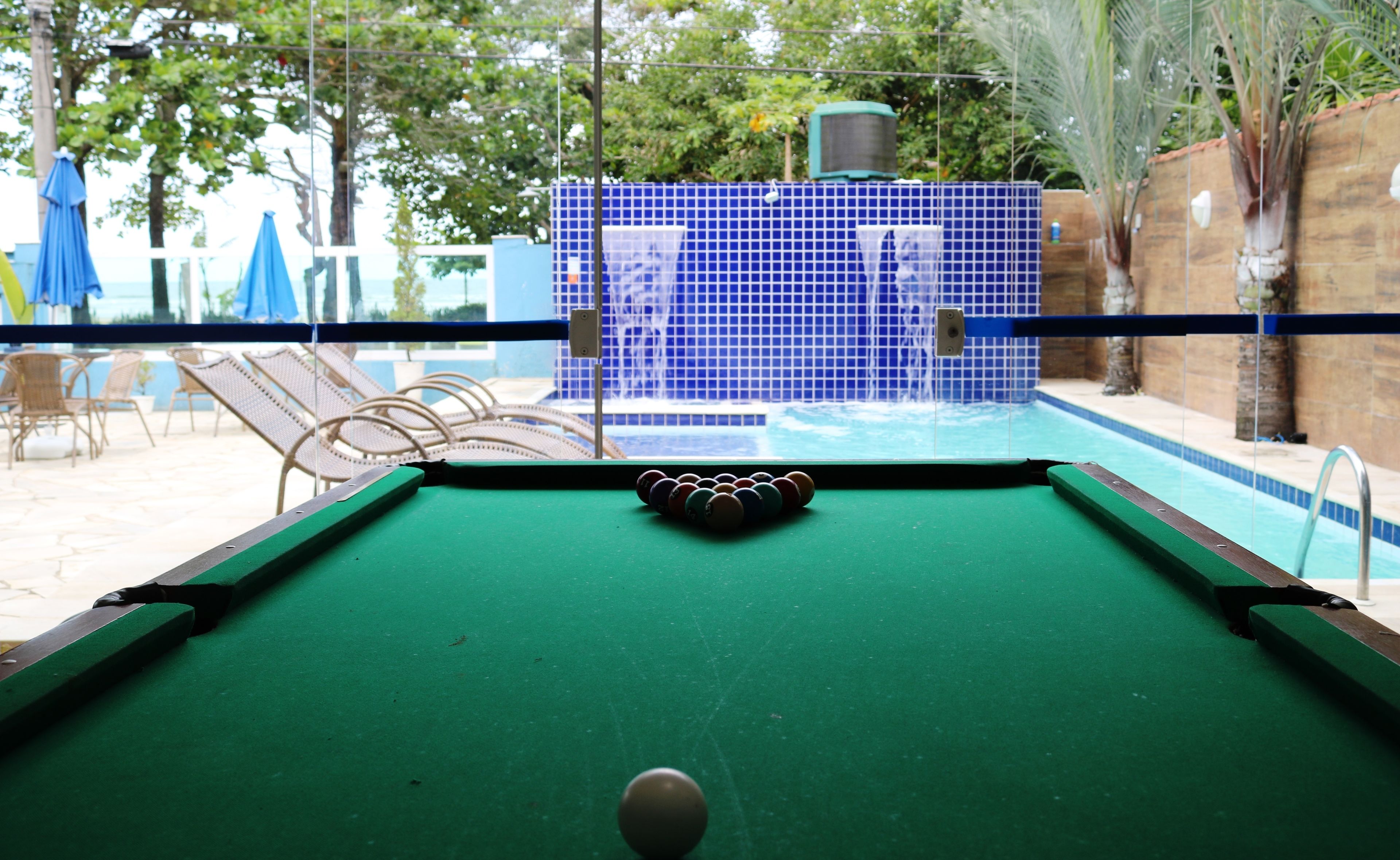 A pool table with a blue tiled backdrop and a pool in the background.