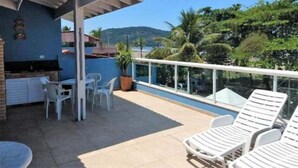 Un balcón con una parrilla, sillas y sillones de relax con vistas a una piscina y zonas verdes.
