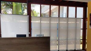 Un área de recepción con un mostrador de madera, un sofá blanco con un cojín azul y un ventanal con paneles de vidrio esmerilado.