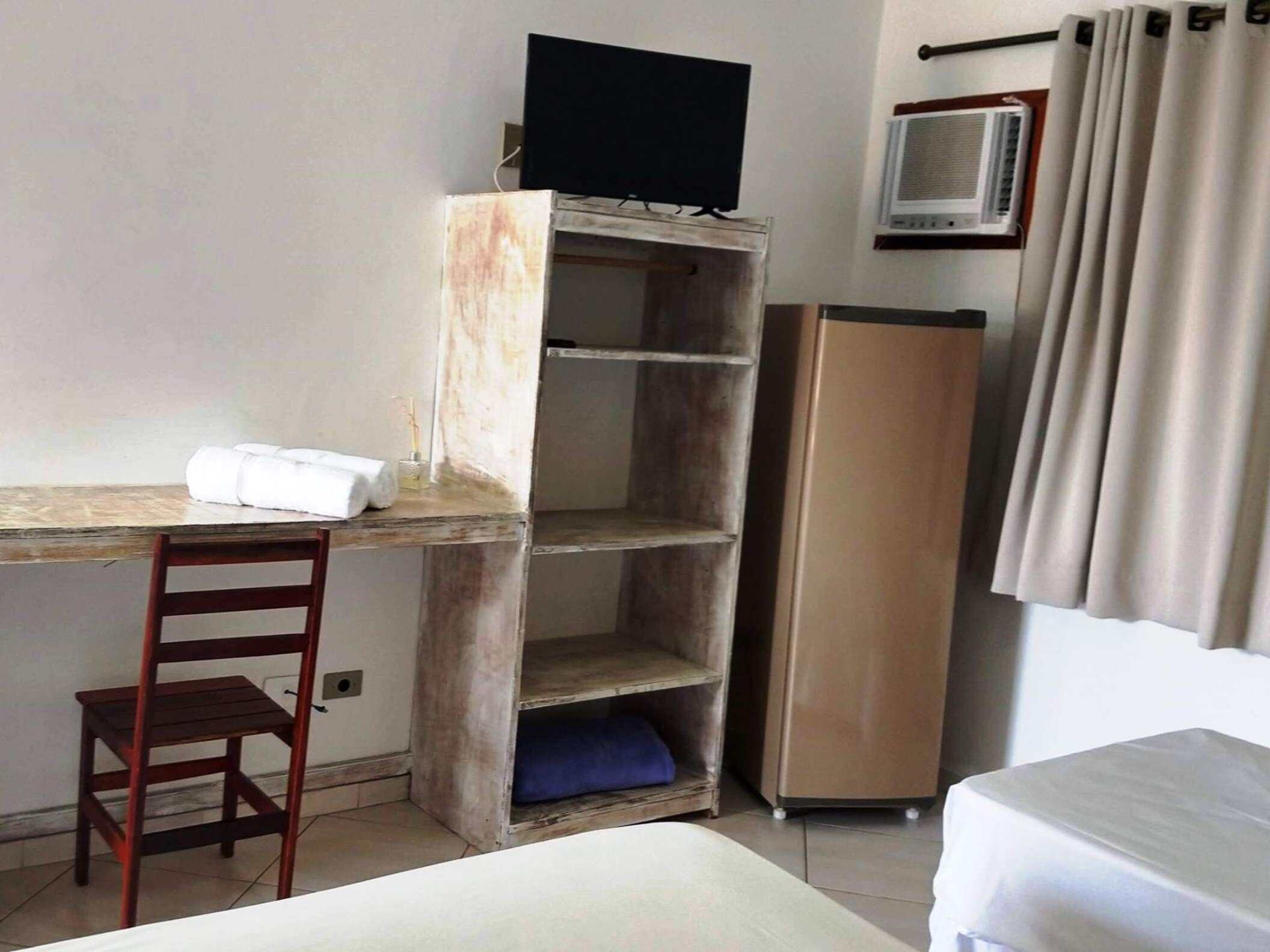 A room with a wooden desk, a chair, a television on a shelf, a wardrobe, and a bed.