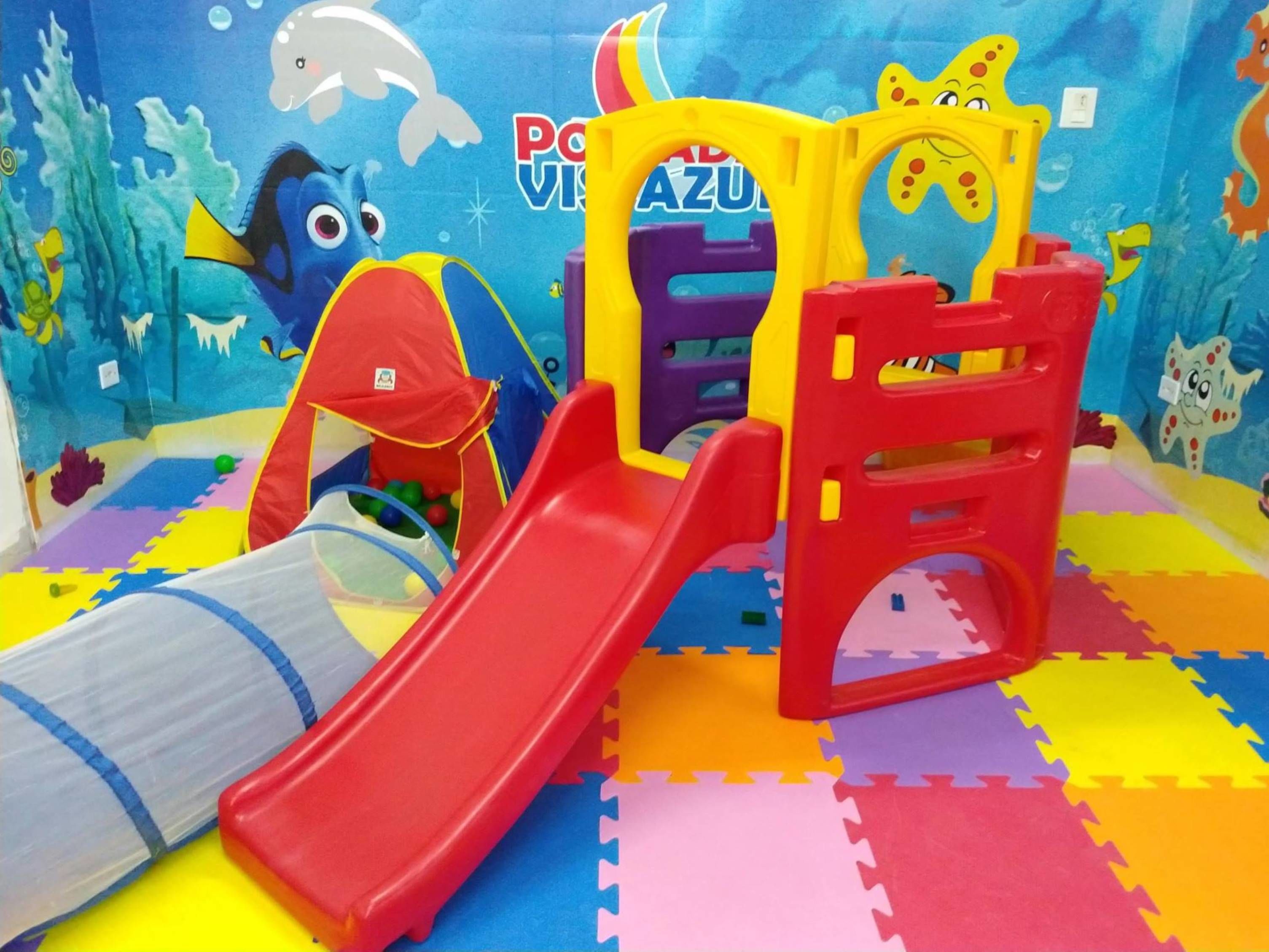Ein Kinderspielbereich mit Rutsche, Klettergerüsten und einem farbenfrohen Boden.