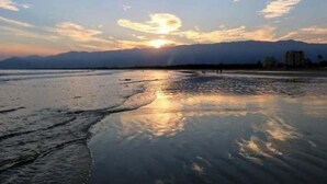 Una playa con un atardecer, agua tranquila y montañas a lo lejos.