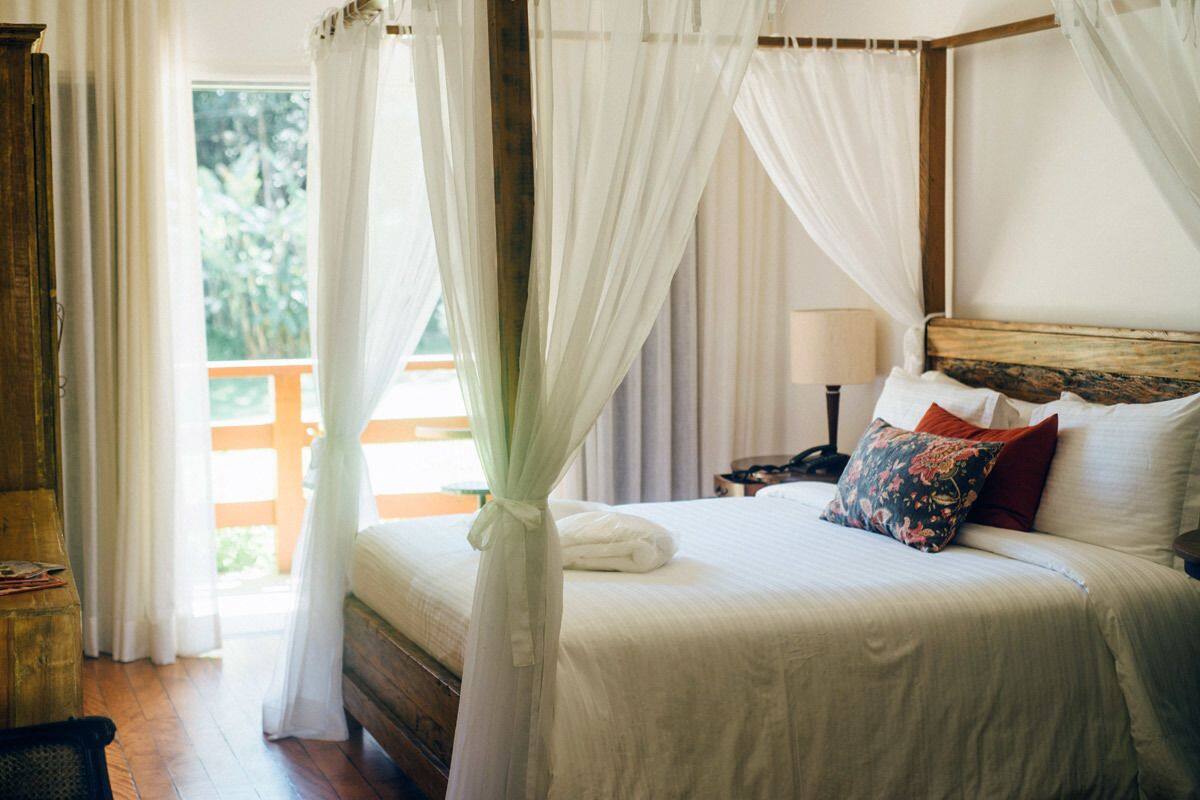 Une chambre à coucher avec un lit à baldaquin, une tête de lit en bois et une vue sur la verdure.