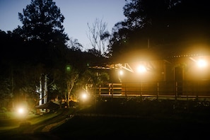 A nighttime view of a building with a wooden structure and a thatched-roof pavilion in a forested area. - Pousada Tucano do Cuiabá (Petrópolis)